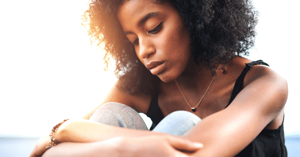A woman is sitting with her arms wrapped around her legs. She is feeling lost.