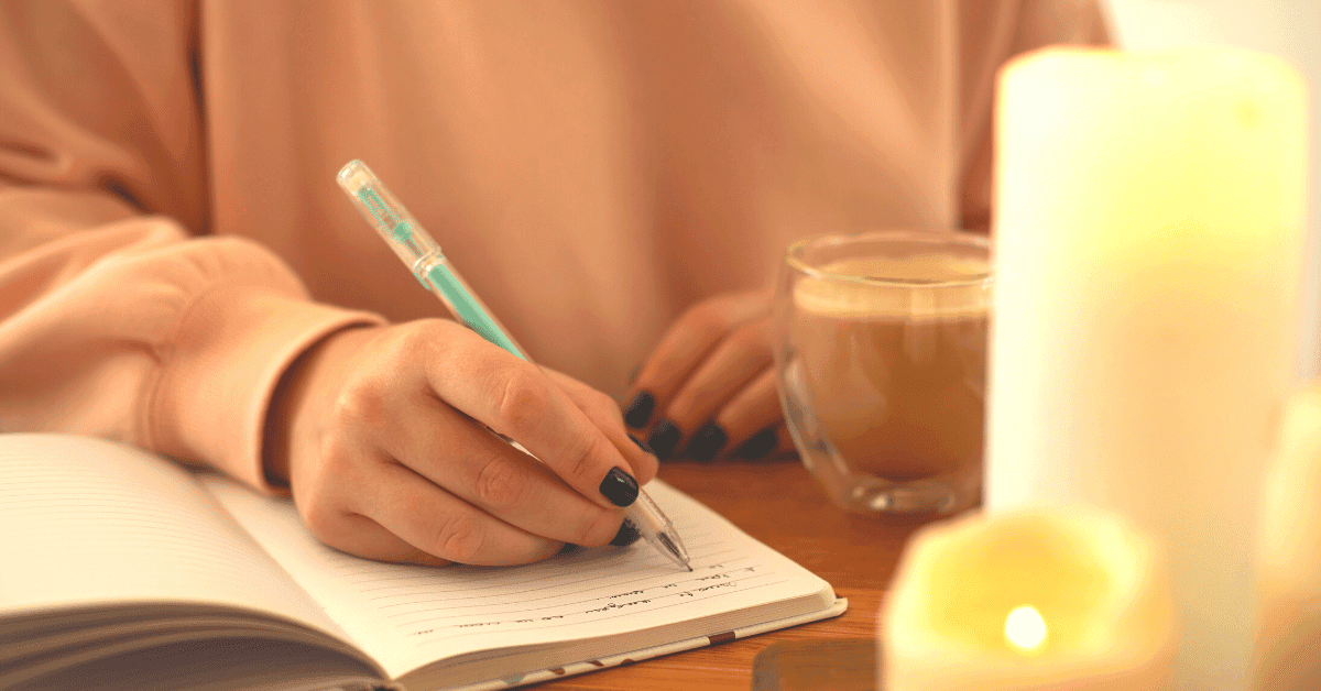 A woman is sitting at a desk with candles and coffee writing in her journal