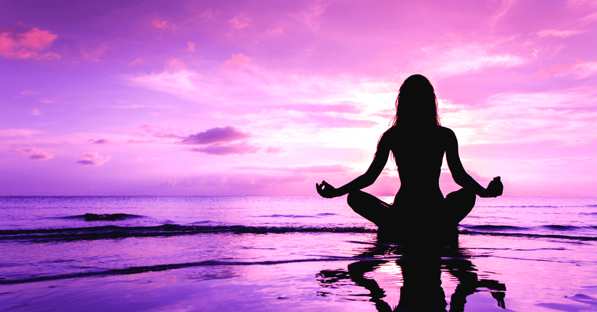 A woman is sitting on the shore in the sunset, meditating